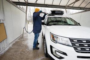 uomo lavaggio alto pressione acqua americano suv auto con tetto cremagliera a se stesso servizio lavare nel freddo tempo atmosferico. foto