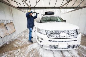uomo lavaggio alto pressione acqua americano suv auto con tetto cremagliera a se stesso servizio lavare nel freddo tempo atmosferico. foto