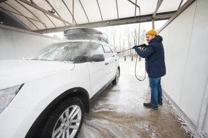 uomo lavaggio alto pressione acqua americano suv auto con tetto cremagliera a se stesso servizio lavare nel freddo tempo atmosferico. foto