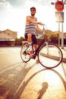 giovane uomo nel occhiali da sole equitazione un' bicicletta su un' città strada a tramonto leggero foto