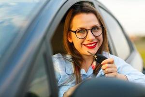 giovane bella donna seduta nel un' auto con il chiavi nel mano foto