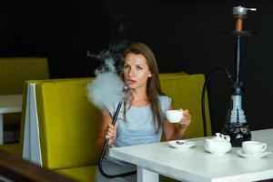 bellissimo donna fumo un' narghilè e potabile tè nel un' bar foto