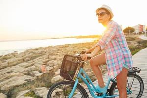 spensierato donna con bicicletta equitazione su un' di legno sentiero a il mare, avendo divertimento e sorridente foto