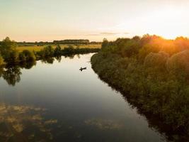 silhouette di un' pescatore nel un' barca su un' fiume a tramonto foto