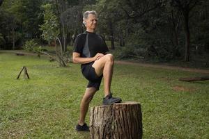 maturo uomo al di fuori a un' Locale parco fare allungamento il suo gamba prima Lavorando su foto