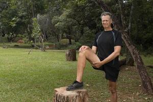 maturo uomo al di fuori a un' Locale parco fare allungamento il suo gamba prima Lavorando su foto