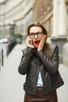sorpreso donna a piedi giù il strada mentre parlando su inteligente Telefono foto