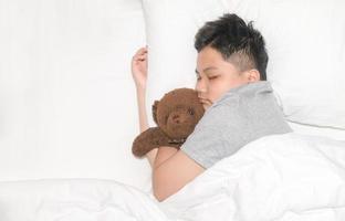 obeso Grasso ragazzo è addormentato con un' orsacchiotto orso nel il suo letto a casa, foto