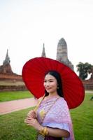 bellissimo tailandese ragazza nel tradizionale vestito costume rosso ombrello come tailandese tempio dove è il pubblico posto, tailandese donna nel tradizionale costume di Tailandia. foto