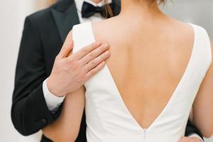 il sposo delicatamente e teneramente abbraccia il sposa di il le spalle. avvicinamento di il mani di un' contento coppia foto