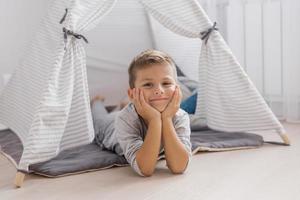 carino bambino è dire bugie su il suo stomaco nel un' tenda-wigwam nel il asilo nel grigio. foto