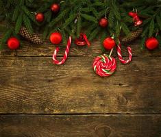 confine di Natale con rami di abete, coni, decorazioni natalizie e bastoncino di zucchero su assi di legno rustici foto