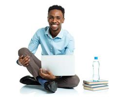 contento africano americano Università alunno con computer portatile, libri e bottiglia di acqua seduta su bianca foto
