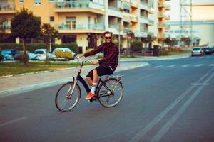 uomo nel occhiali da sole equitazione un' bicicletta su città strada foto