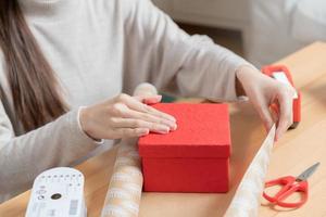 preparare Natale vigilia Festival stagione, mano di asiatico giovane donna, ragazza decorare, involucro carta regalo con rosso scatola, contento per ottenere presente su allegro natale. celebrazione decorazione su nuovo anno giorno le persone. foto