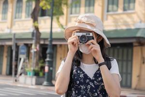 viaggiatore, viaggio asiatico giovane donna o ragazza uso telecamera prendere foto, vecchio cittadina strada, città turismo su contento soleggiato giorno. zaino in spalla turista, vacanza viaggio, estate o vacanza, passatempo concetto. foto