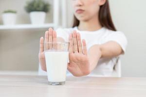 allergia asiatico giovane donna, ragazza mano nel negare, no o spingere su per evitare per bevanda latte a casa, infelice e cattivo stomaco dolore. lattosio intolleranza e latteria cibo, Salute problema, pancia soffrire concetto. foto