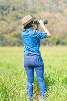 donna indossare cappello e hold binoculare nel erba campo foto