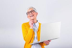 Immagine di allegro maturo donna in piedi isolato al di sopra di grigio sfondo utilizzando il computer portatile computer. ritratto di un' sorridente anziano signora Tenere il computer portatile computer foto