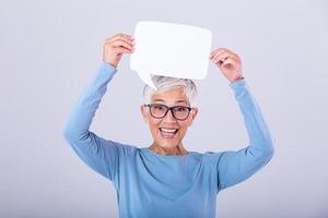 allegro maturo donna Tenere discorso bolla cartello al di sopra di sua testa e sorridente. contento anziano signora con discorso bolla bandiera donna mostrando cartello discorso bolla bandiera guardare contento foto