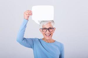 allegro maturo donna Tenere discorso bolla cartello al di sopra di sua testa e sorridente. contento anziano signora con discorso bolla bandiera foto