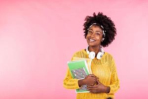 attraente giovane alunno sorridente a telecamera con libri e cuffia. africano americano donna Tenere i Quaderni. formazione scolastica concetto foto