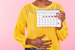 ritagliata tiro malattia donna Tenere periodi calendario per controllo mestruazione giorni mettere mano su pancia isolato su rosa sfondo. medico, assistenza sanitaria, ginecologico concetto. copia spazio foto