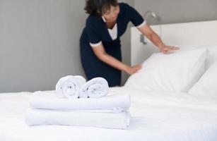 Hotel camera servizio. giovane domestica fabbricazione letto nel un' camera, messa a fuoco di pulito asciugamani foto