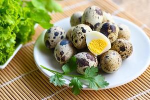 bollito uova cibo, Quaglia uova su bianca piatto, prima colazione uova con fresco Quaglia uova e verdura coriandolo su di legno tavolo sfondo foto