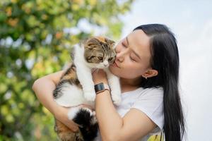 asiatico donna con lungo nero capelli abbracciare sua animale domestico con un' Sorridi. lei è giocando con un' gatto. animali domestici e stile di vita concetto. foto