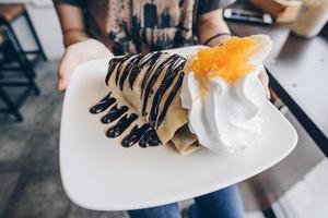 il dolce dolce cioccolato Banana crepes con oro discussioni guarnizione e un' tazza di caldo latte macchiato caffè. foto