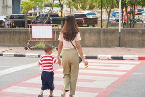 madre prende sua bambino per camminare attraverso il strada. foto