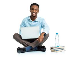 contento africano americano Università alunno con computer portatile, libri e bottiglia di acqua seduta su bianca foto