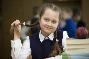 divertente scolara con trecce. ragazza nel il aula con libri e un Mela. secondario scuola. indietro per scuola. foto