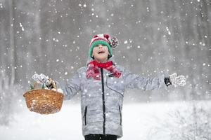 un' contento bambino nel il inverno foresta gioisce nel il neve. poco ragazzo nel un' a strisce Natale cappello sotto il neve. foto