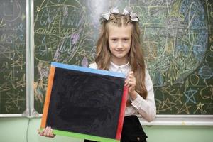 scolara di mezzo scuola età nel il aula Tenere un' disegno tavola e guardare a il telecamera. foto