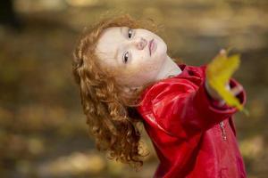 bellissimo poco dai capelli rossi ragazza con acero le foglie all'aperto foto