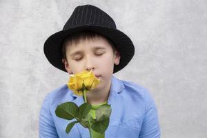 ritratto di un' ragazzo nel un' cappello e completo da uomo con un' rosa. bambino con fiore per La madre di giorno o vacanza. elegante divertente uomo con un' fiore per un' regalo. foto