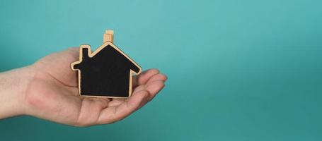 piccolo legna Casa nel mani rappresentare concetti come come casa cura famiglia amore vero tenuta alloggiamento riparo assicurazione e mutuo. mani Tenere piccolo modello Casa isolato su blu verde studio sfondo. foto