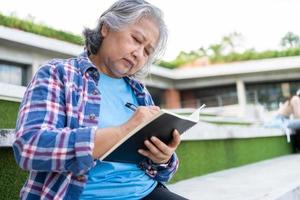 maturo adulto alunno seduta nel davanti via Università edificio e lettura scuola libri dopo frequentando un' Università classe, adulto formazione scolastica apprendimento studiando contento asiatico anziano pensionato attività foto