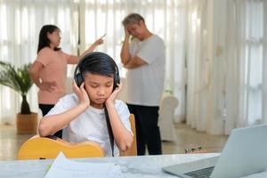 ragazzo asiatico che indossa le cuffie e suona musica ad alto volume. in modo da non sentire litigare mentre i genitori litigano o litigano in casa. problema infelice in famiglia, problemi domestici in famiglia. foto