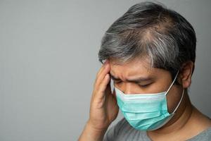 uomo asiatico malato che indossa una maschera medica e prende una mano per tenere il mal di testa nella testa. concetto di protezione da coronavirus pandemico e malattie respiratorie foto