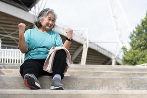 contento e Sorridi anziano asiatico donna seduta su le scale per riposo dopo allenamento, jogging su mattina, anziano esercizio all'aperto per bene sano. concetto di assistenza sanitaria e attivo stile di vita per salutare foto