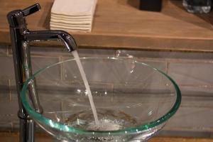 acqua bicchiere Lavello a partire dal il rubinetto il bagno. foto