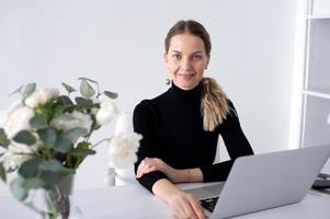 il ragazza lavori nel un' bianca ufficio con un' il computer portatile e fiori su il tavolo foto