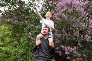 il ragazzo è seduta su di papà le spalle, puntamento il suo dito per il lato e ridendo foto