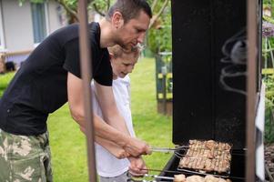 allegro papà e figlio arrosto carne su il griglia foto