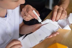 un' carino ragazzo è seduta con il suo papà a il tavolo e raccolta origami foto