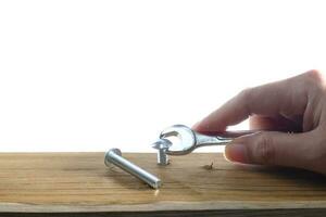 una mano utilizzando una chiave avvitando una vite in una tavola di legno su uno sfondo bianco foto