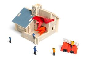 vigili del fuoco in miniatura che si prendono cura di un'emergenza incendio in una casa di legno foto